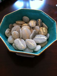 a bowl full of rocks with writing on them sitting on top of a wooden table