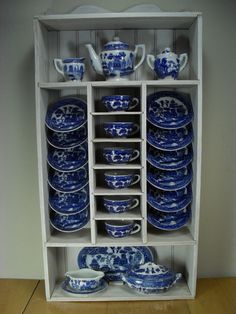 a shelf filled with blue and white china on top of a wooden floor next to a wall