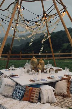 an outdoor table set with plates and place settings in front of a wooden structure decorated with string lights