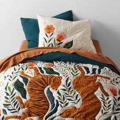 a bed with an orange and blue comforter on top of it next to a white wall