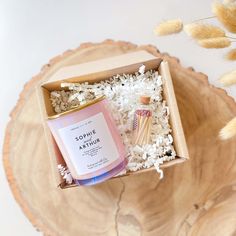 an open box containing two candles and rice on a wooden table next to dried flowers