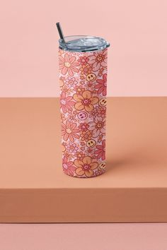 a pink and orange flowered cup with a straw in it on a tan surface