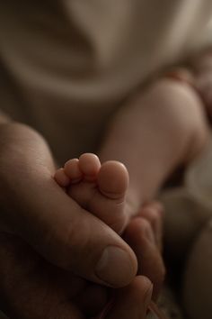 a close up of a person holding a baby's hand with both hands on it