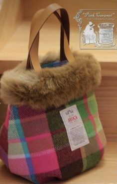 a plaid bag with a fur collar hanging from it's side on a wooden shelf