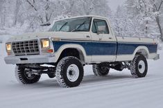 a white and blue truck driving down a snow covered road with trees in the background