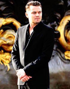 a man in a black suit and tie standing next to a golden dragon sculpture with his hand on his hip