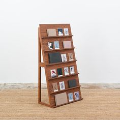 a wooden book shelf with many books on it and pictures hanging from the top, in front of a white wall