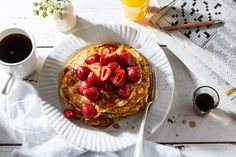 pancakes with strawberries and syrup on a white plate next to a cup of coffee