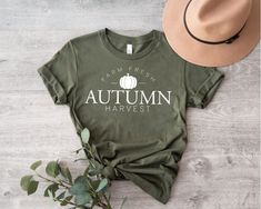 a t - shirt with the words autumn harvest on it next to a hat