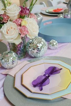 the table is set with disco balls, plates and vases filled with pink flowers