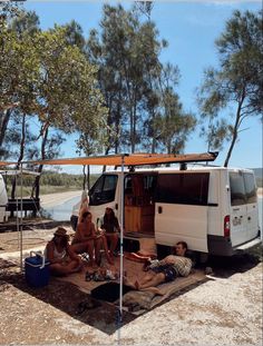 some people are sitting on the ground near a van with a awning over it