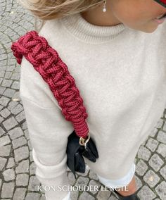 a woman wearing black gloves and a red crochet tie around her neck is looking down at the ground