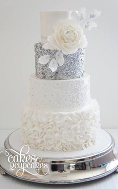 a three tiered wedding cake with white flowers and silver sequins on top