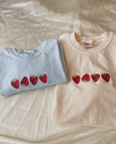 two t - shirts with strawberries on them are sitting on a white bed sheet