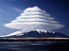 there is a very large cloud in the sky over a mountain with snow on it