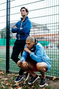 two men standing next to each other in front of a fence