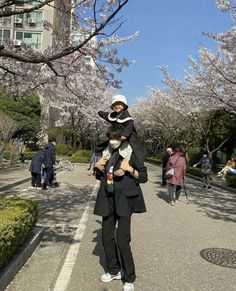 a woman holding a baby in her arms while walking down a street lined with cherry blossom trees