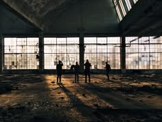 several people standing in an abandoned building looking out the windows at the sun coming through