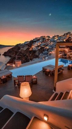 the sun is setting over an outdoor pool with lounge chairs and lights in front of it