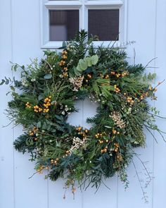 a wreath hanging on the side of a white door with yellow berries and greenery