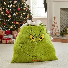 a green grin face pillow sitting on top of a white rug next to a christmas tree