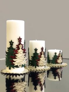 three candles with christmas trees on them are sitting on a glass table and reflected in the water