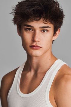 a young man wearing a white tank top and looking at the camera with a serious look on his face