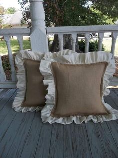 two pillows sitting on top of a wooden porch next to a white fence and trees