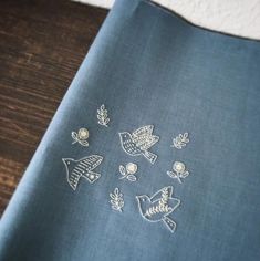 a blue table cloth with embroidered birds and leaves on it, sitting on a wooden surface