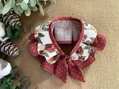 a red and white flowered bow tie sitting on top of a table next to pine cones