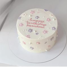 a white cake with pink and purple flowers on it sitting on a plate next to a knife