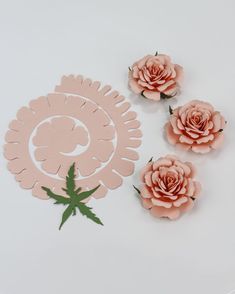 three pink paper flowers sitting next to each other on a white surface with green leaves