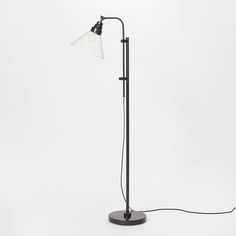 a black and white floor lamp with a glass shade on the top, standing in front of a white wall