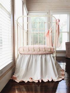 a white crib with pink ruffled bedding in front of a large window