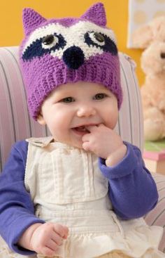 a baby wearing a knitted hat sitting in a chair next to a teddy bear