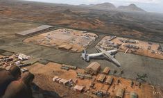 an airplane is flying over the desert with other vehicles and buildings in the foreground