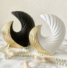 two white and black vases sitting on top of a marble table next to pearls