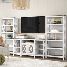 a living room with white bookcases and a large tv on top of it