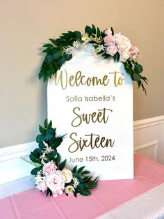 a welcome sign on top of a table with flowers and greenery in front of it