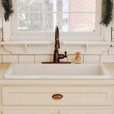 a white kitchen sink under a window with wreaths on the windowsill above it