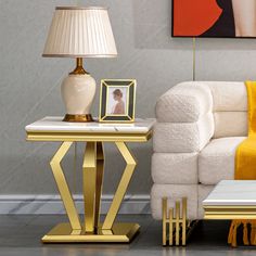 a white couch sitting next to a table with a lamp and pictures on the wall