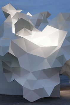 an abstract white sculpture is shown against the blue sky and water in this image, it appears to be made out of polygonic shapes