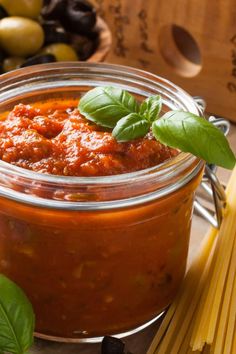 a glass jar filled with marinara sauce next to pasta and olives