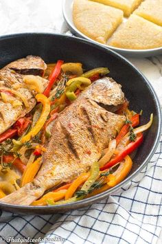 fish and vegetables in a skillet with bread on the side