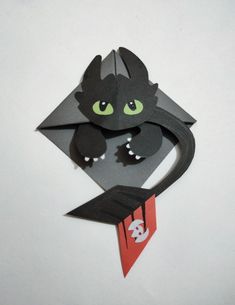 an origami cat with green eyes holding a red tag on it's tail