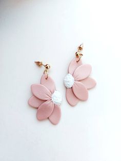 two pink and white flower shaped earrings with gold chains hanging from each earring on a white surface