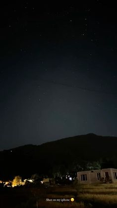 the night sky is lit up with stars above some houses and hills in the distance