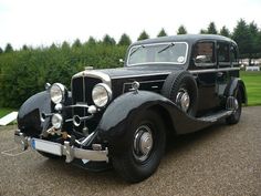 an old black car is parked on the gravel