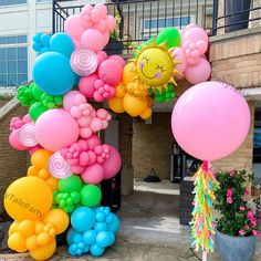 an arch made out of balloons in front of a building with flowers on the ground