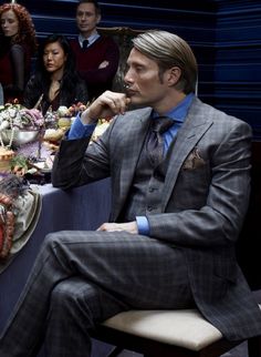 a man in a suit sitting at a table with other people around him eating food